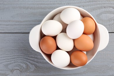 Unpeeled boiled eggs in saucepan on grey wooden table, top view