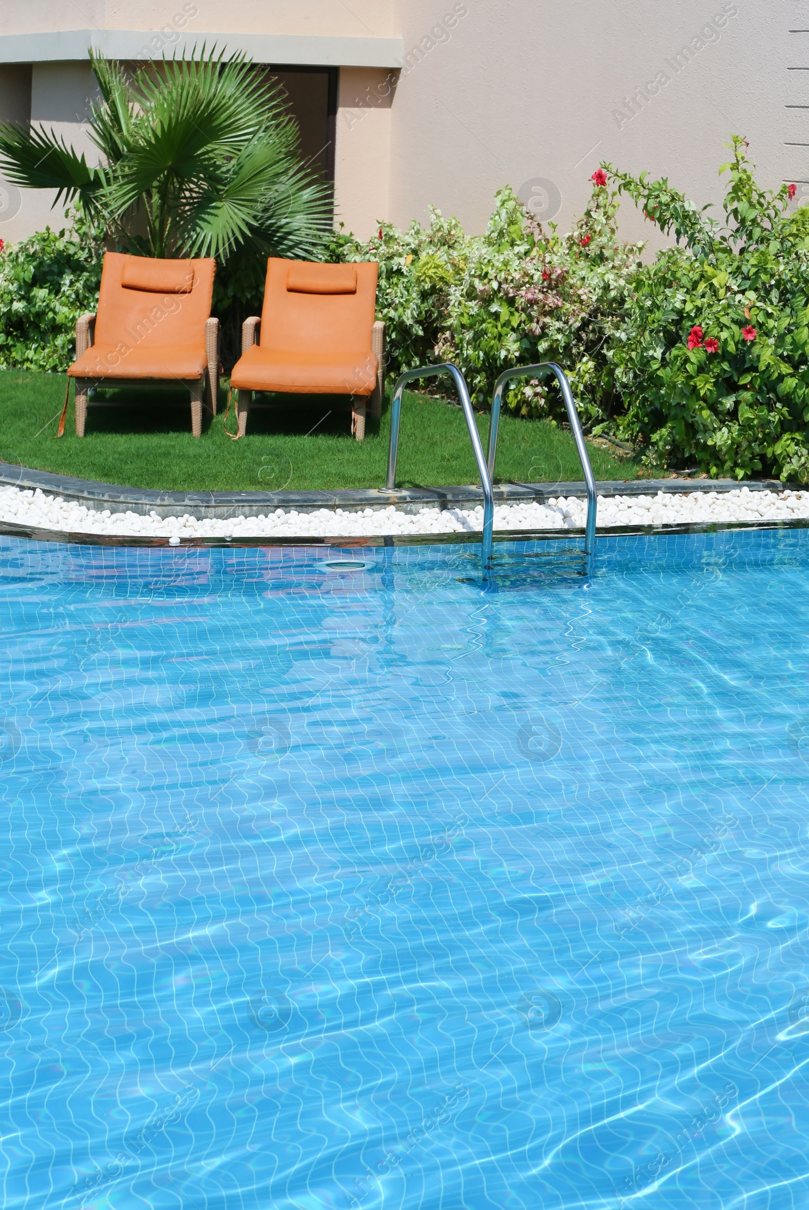 Photo of Sunbeds near modern swimming pool with stairs, outdoors