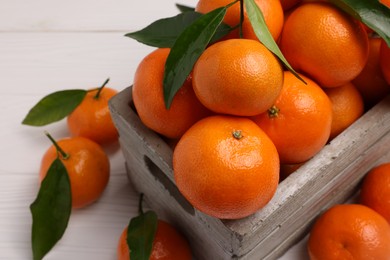 Photo of Delicious tangerines with leaves in crate on white wooden table, closeup