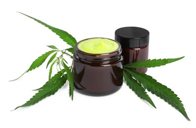 Photo of Jars with hemp cream and green leaves on white background. Natural cosmetics