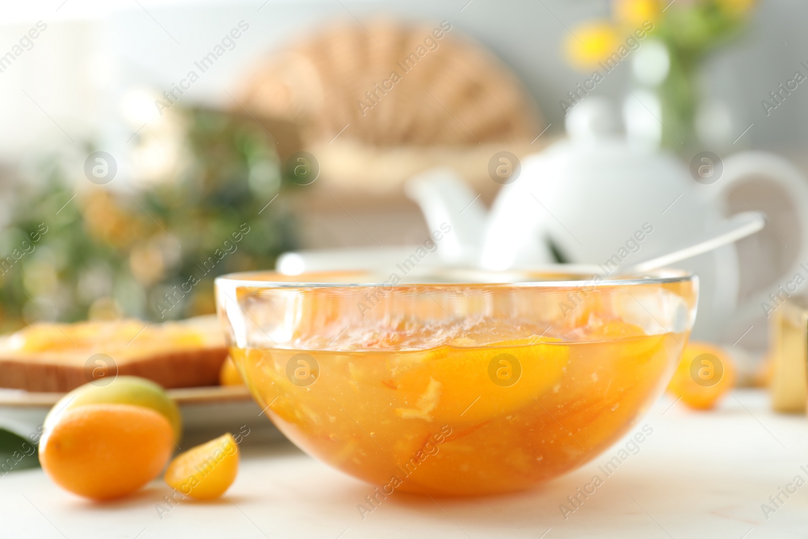 Photo of Delicious kumquat jam in glass bowl on white table, closeup