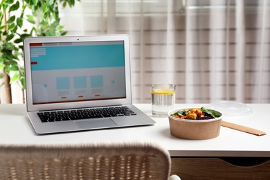 Photo of Delicious salad with chicken and vegetables near laptop on white table indoors