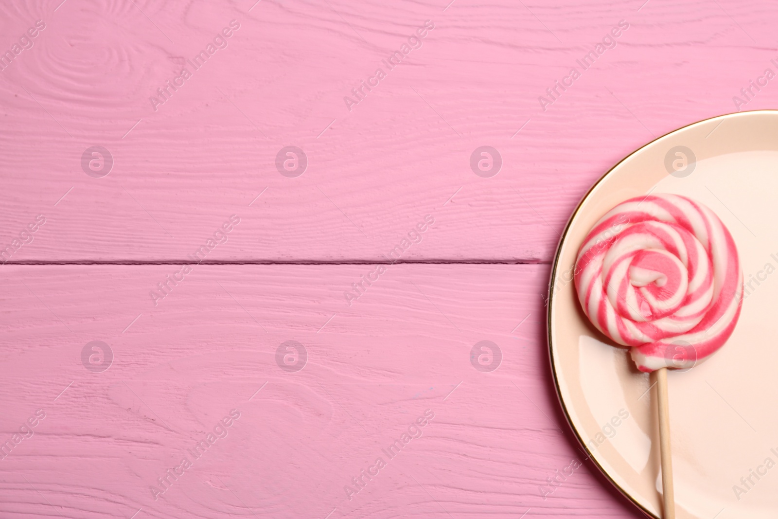 Photo of Plate with tasty sweet lollipop on pink wooden table, top view. Space for text