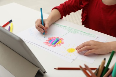 Photo of Little girl drawing on paper with pencil at online lesson indoors, closeup. Distance learning