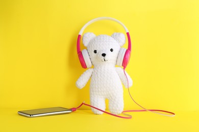 Photo of Baby songs. Toy bear in headphones and smartphone on yellow background