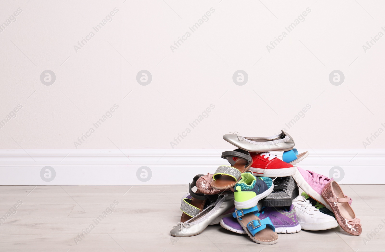 Photo of Heap of different shoes on floor against light wall. Space for text