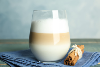 Delicious latte macchiato and cinnamon on wooden table against light blue background