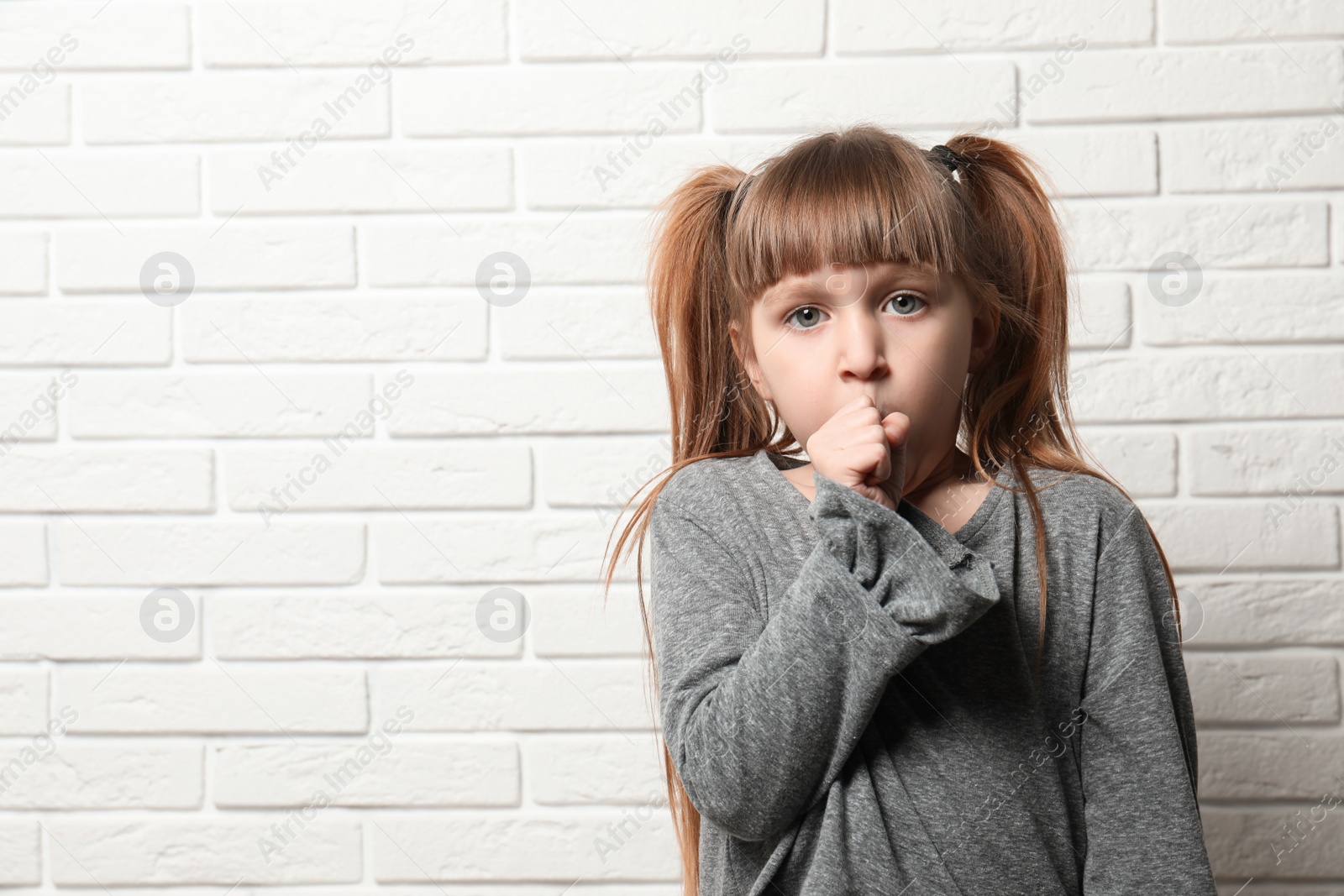 Photo of Cute little girl coughing near brick wall. Space for text