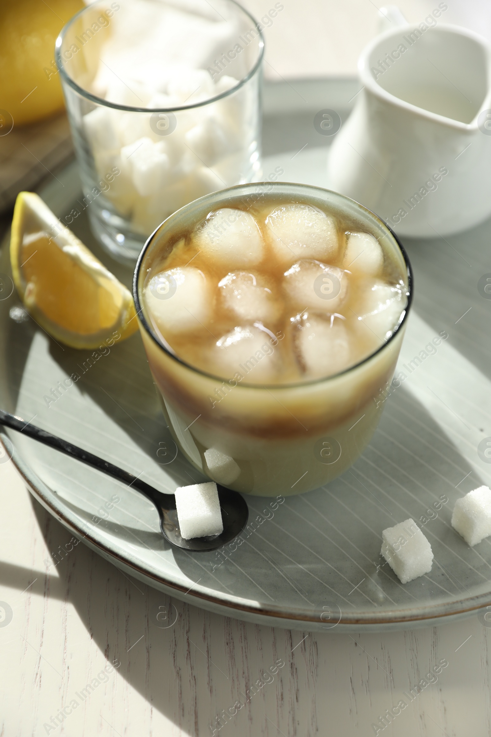 Photo of Refreshing iced coffee with milk in glass, sugar cubes and spoon on white wooden table