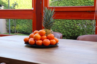 Photo of Fresh tangerines and pineapple on wooden table indoors