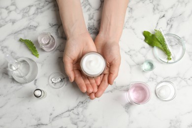 Photo of Woman holding jar of cosmetic product at white marble table, top view