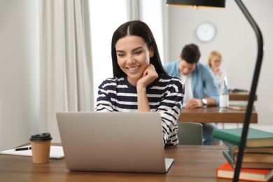 Photo of Young woman with laptop studying at table in library