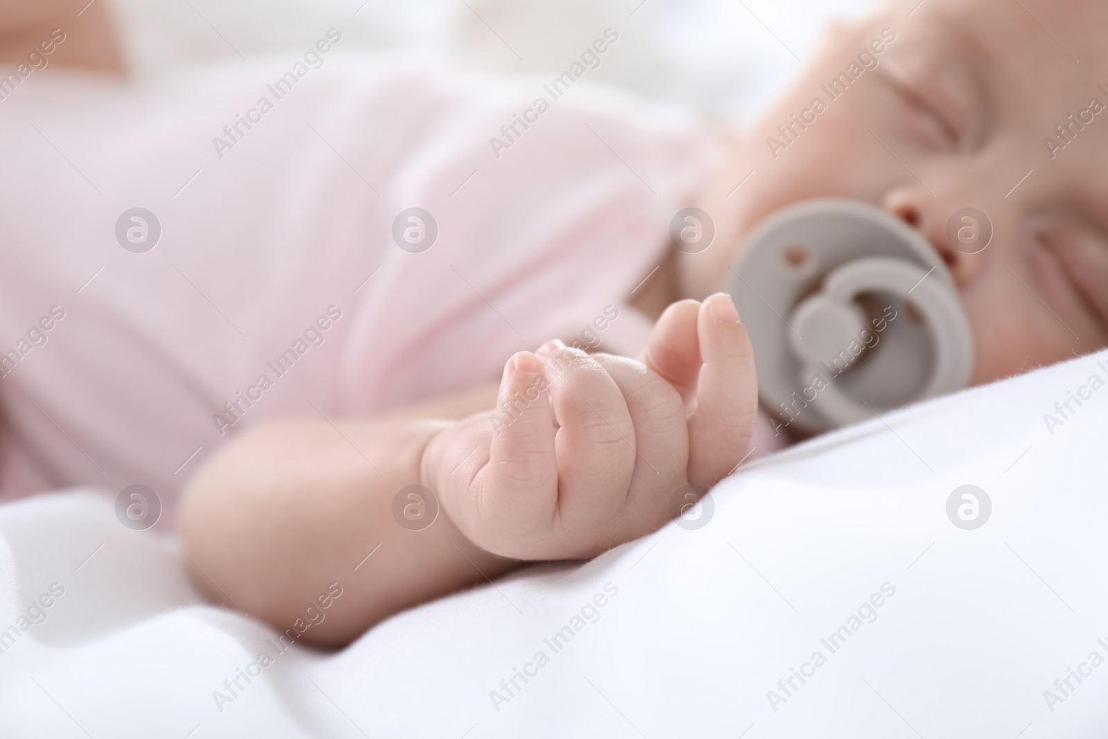 Photo of Cute little baby with pacifier sleeping at home, focus on hand