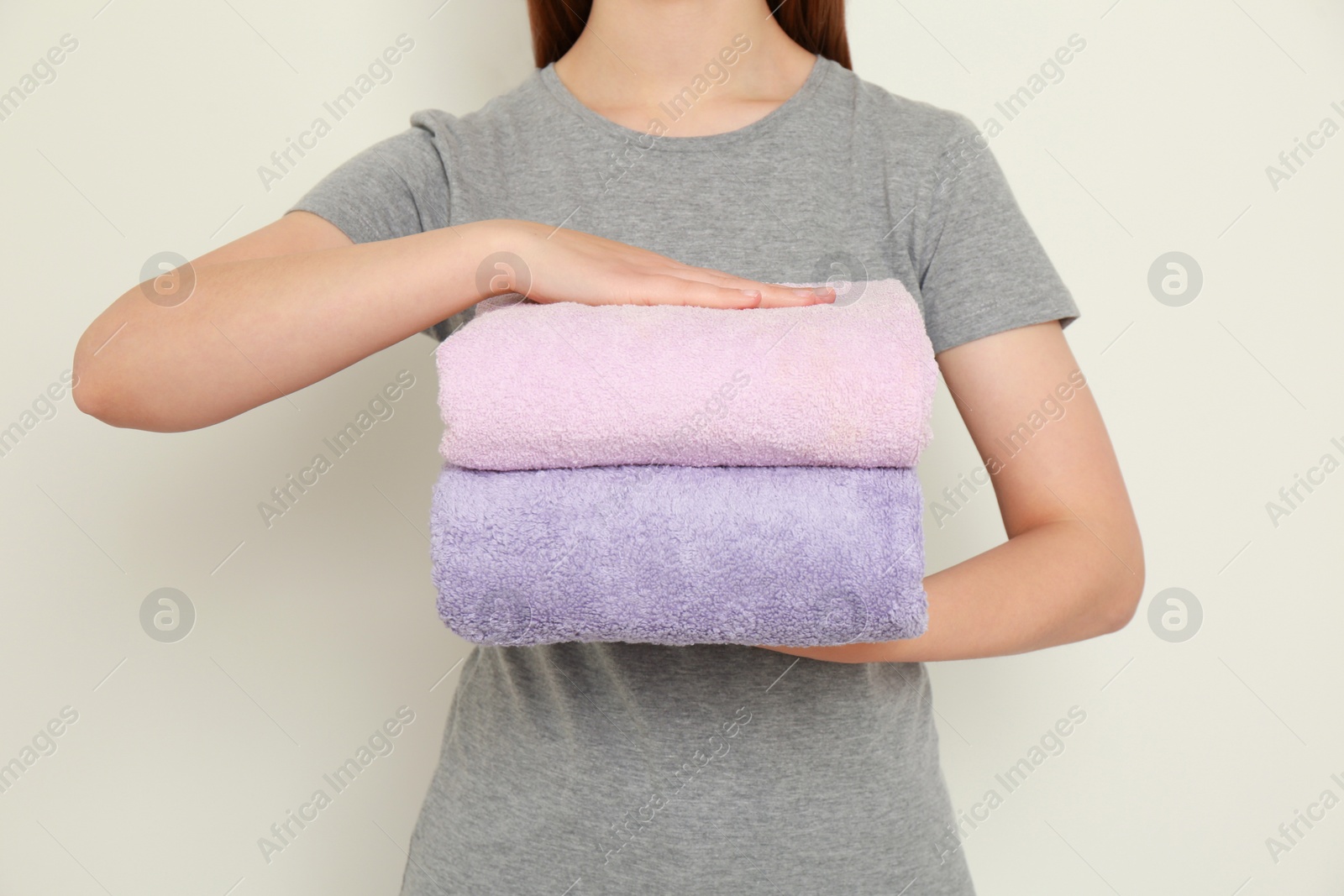 Photo of Woman holding folded soft terry towels on light background, closeup