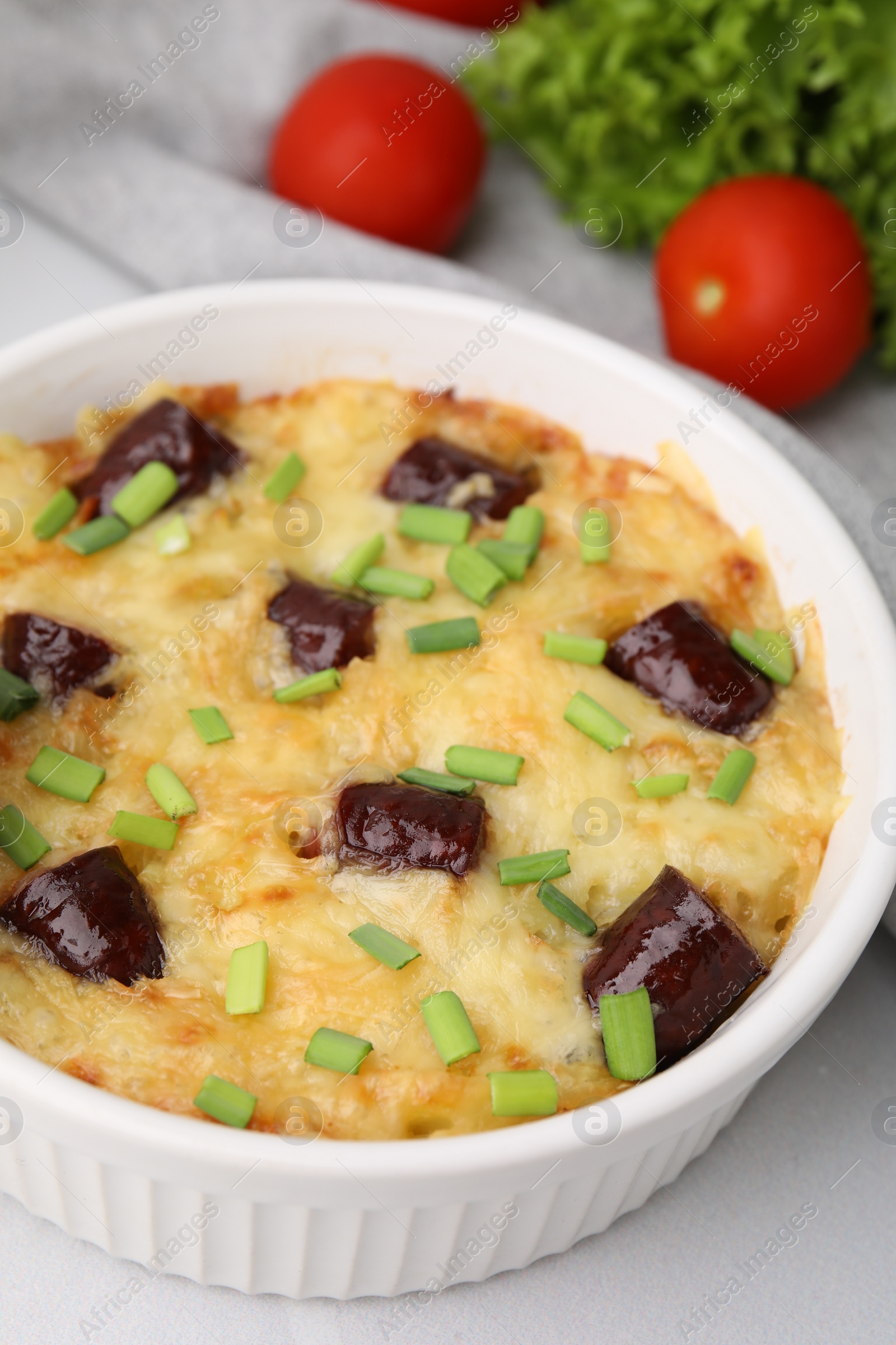 Photo of Tasty sausage casserole with green onions in baking dish served on white tiled table, closeup