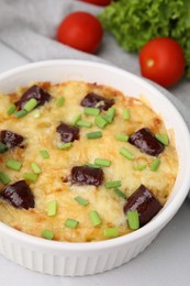 Photo of Tasty sausage casserole with green onions in baking dish served on white tiled table, closeup