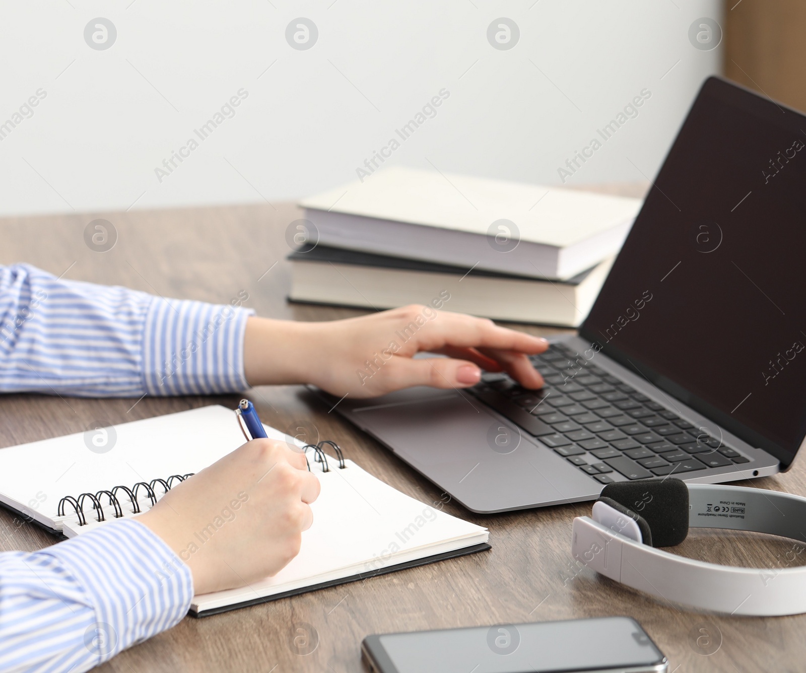 Photo of E-learning. Woman taking notes during online lesson at table indoors, closeup