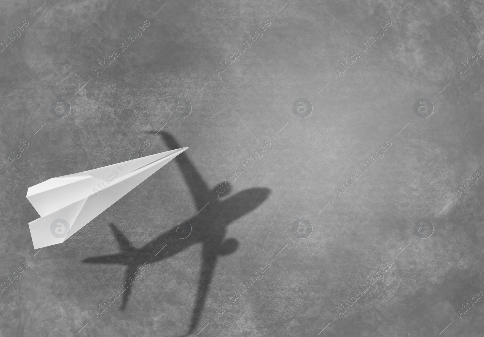 Image of Flying paper plane and shadow of a real airplane on asphalt