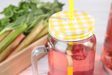 Mason jar of tasty rhubarb cocktail with raspberry on table, closeup