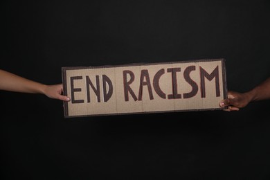 Photo of Woman and African American man holding sign with phrase End Racism on black background, closeup