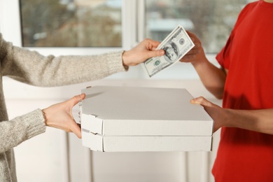 Young woman giving money to pay for food delivery indoors, closeup. Ordering pizza