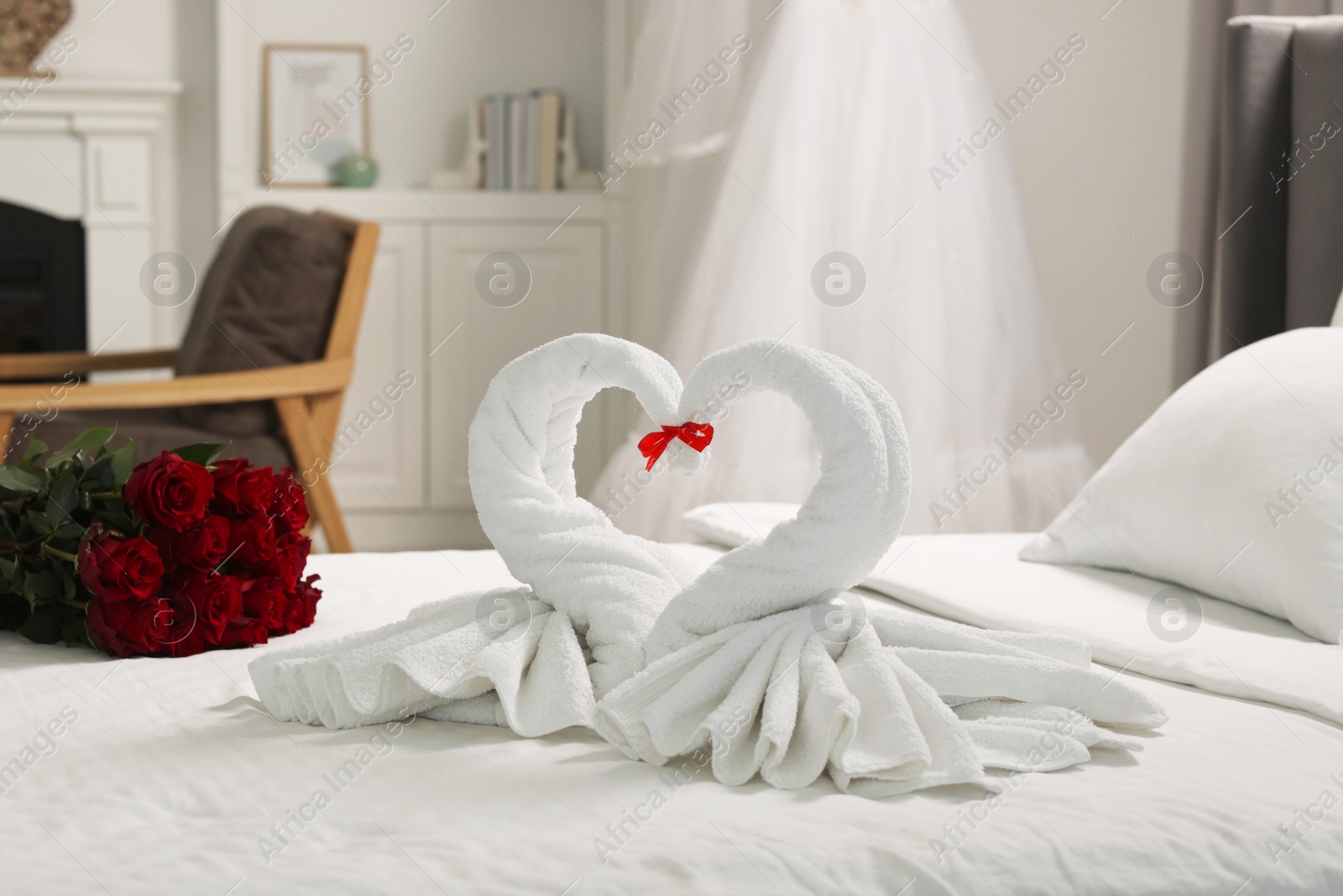 Photo of Honeymoon. Swans made of towels and beautiful red roses on bed in room