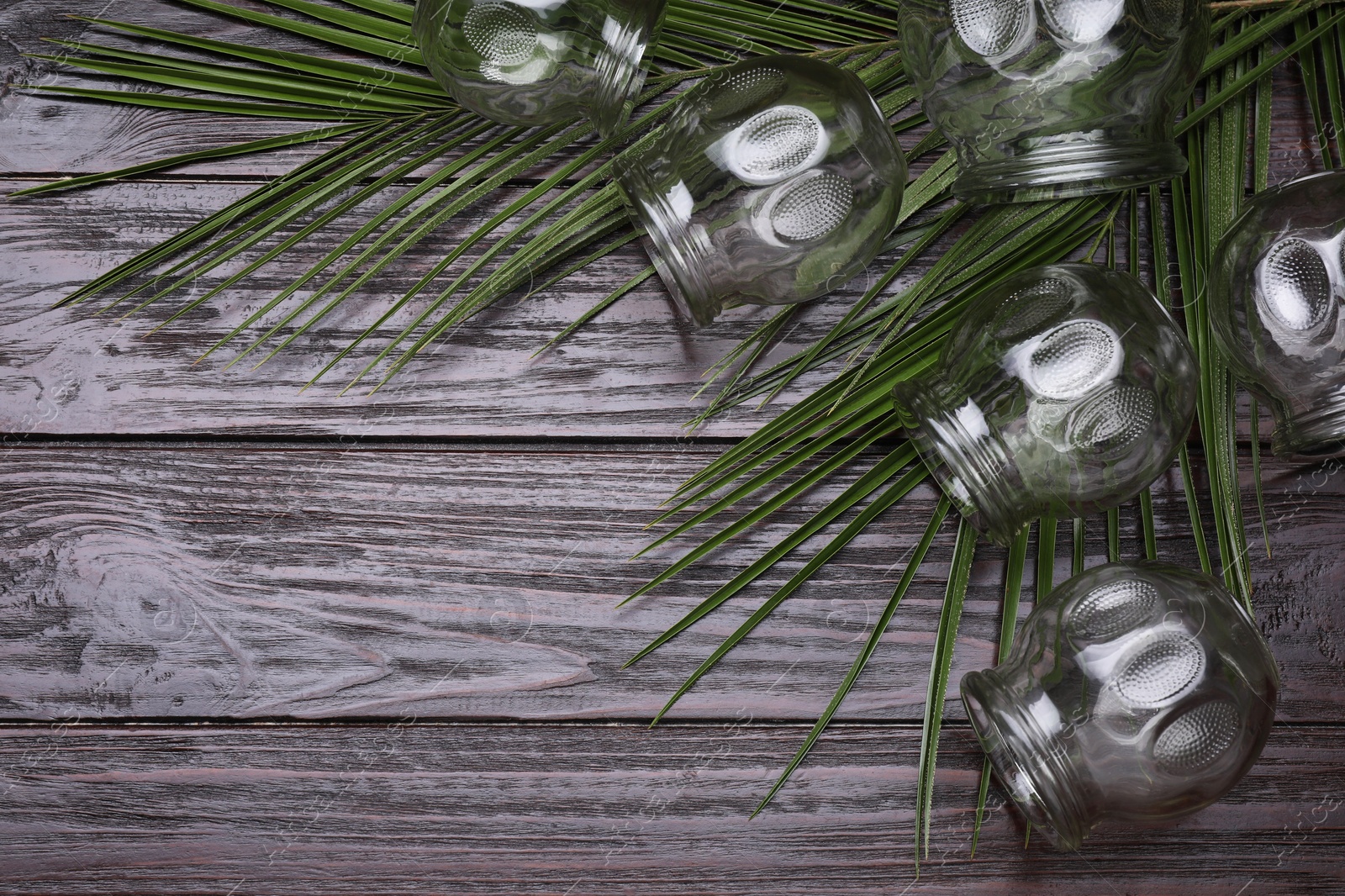 Photo of Glass cups and green leaves on wooden table, flat lay with space for text. Cupping therapy