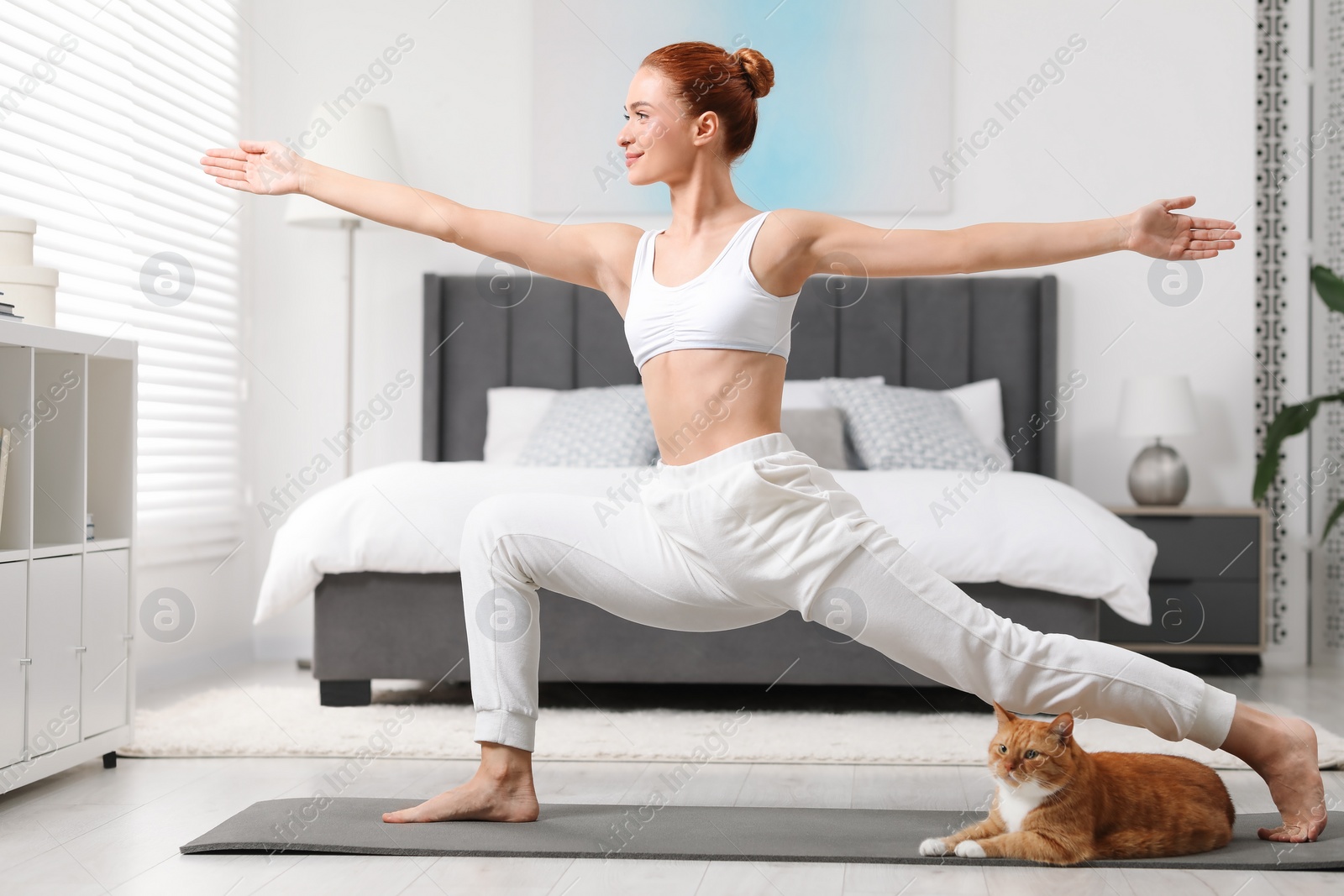 Photo of Beautiful woman with cute red cat practicing yoga on mat at home