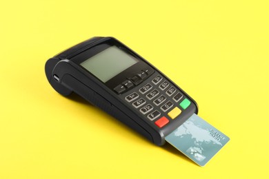 Photo of New modern payment terminal with credit card on yellow background