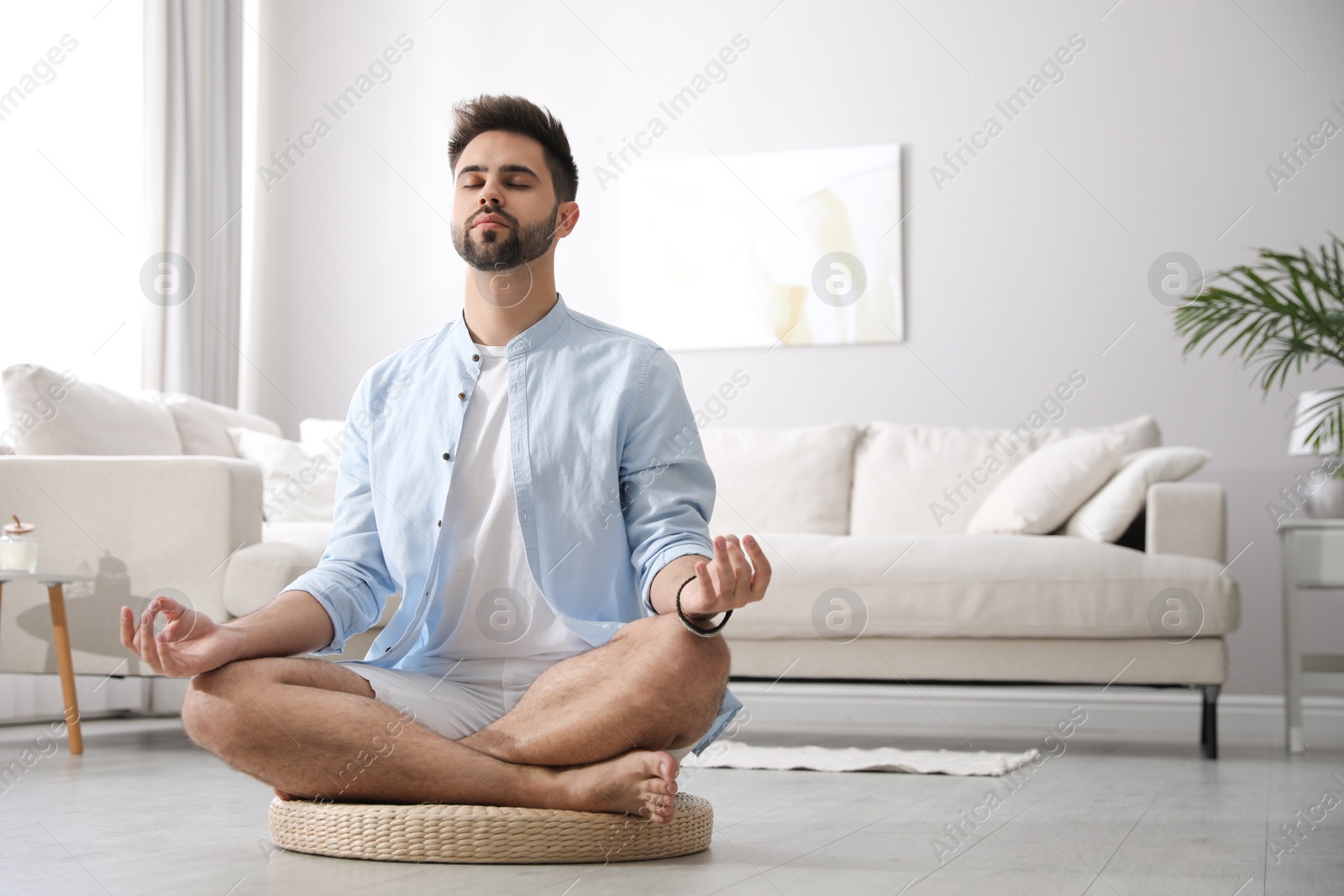 Photo of Young man meditating on straw cushion at home, space for text