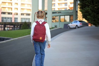 Photo of Cute little girl with backpack on city street back view. Space for text