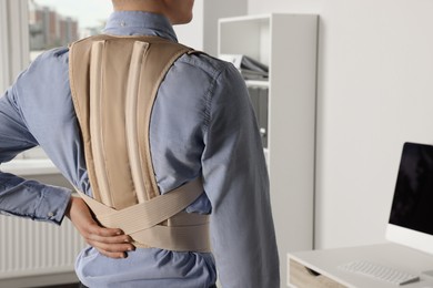 Closeup of man with orthopedic corset in room, back view