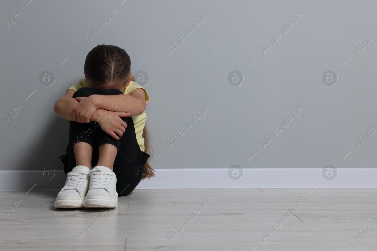 Photo of Child abuse. Upset girl sitting on floor near grey wall, space for text