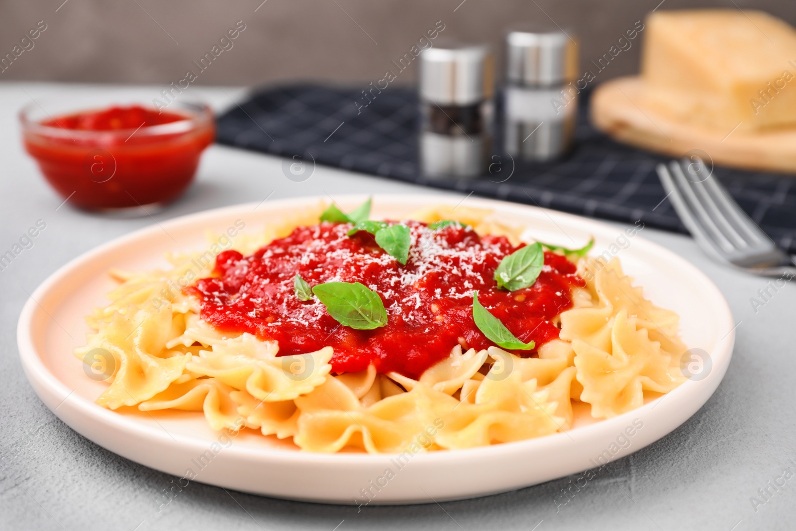 Photo of Tasty pasta with tomato sauce, basil and cheese on light grey table, closeup