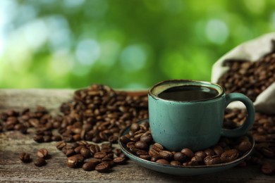 Image of Cup of aromatic hot coffee and beans on wooden table outdoors 