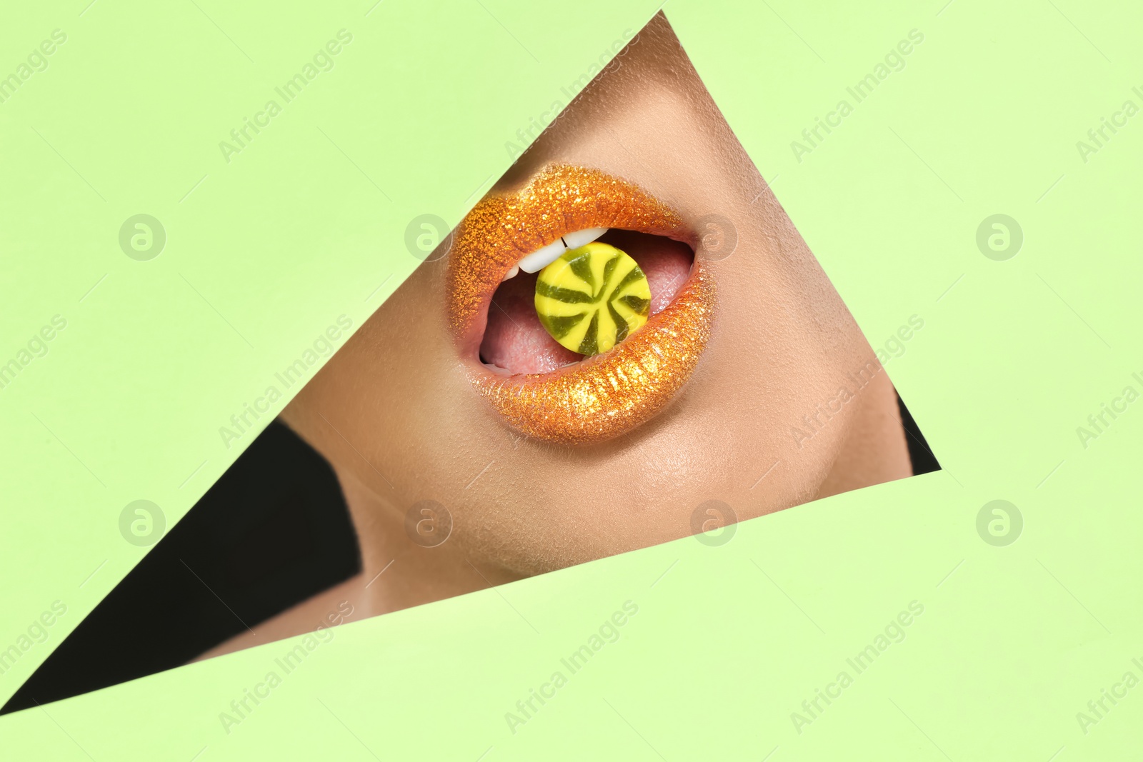 Photo of View of beautiful young woman with creative lips makeup and candy through cutout in color paper