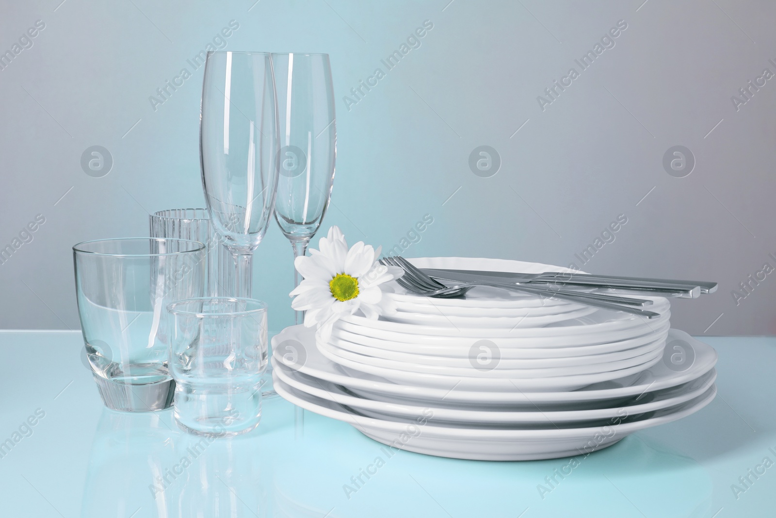 Photo of Set of clean dishes, glasses and cutlery on light blue table