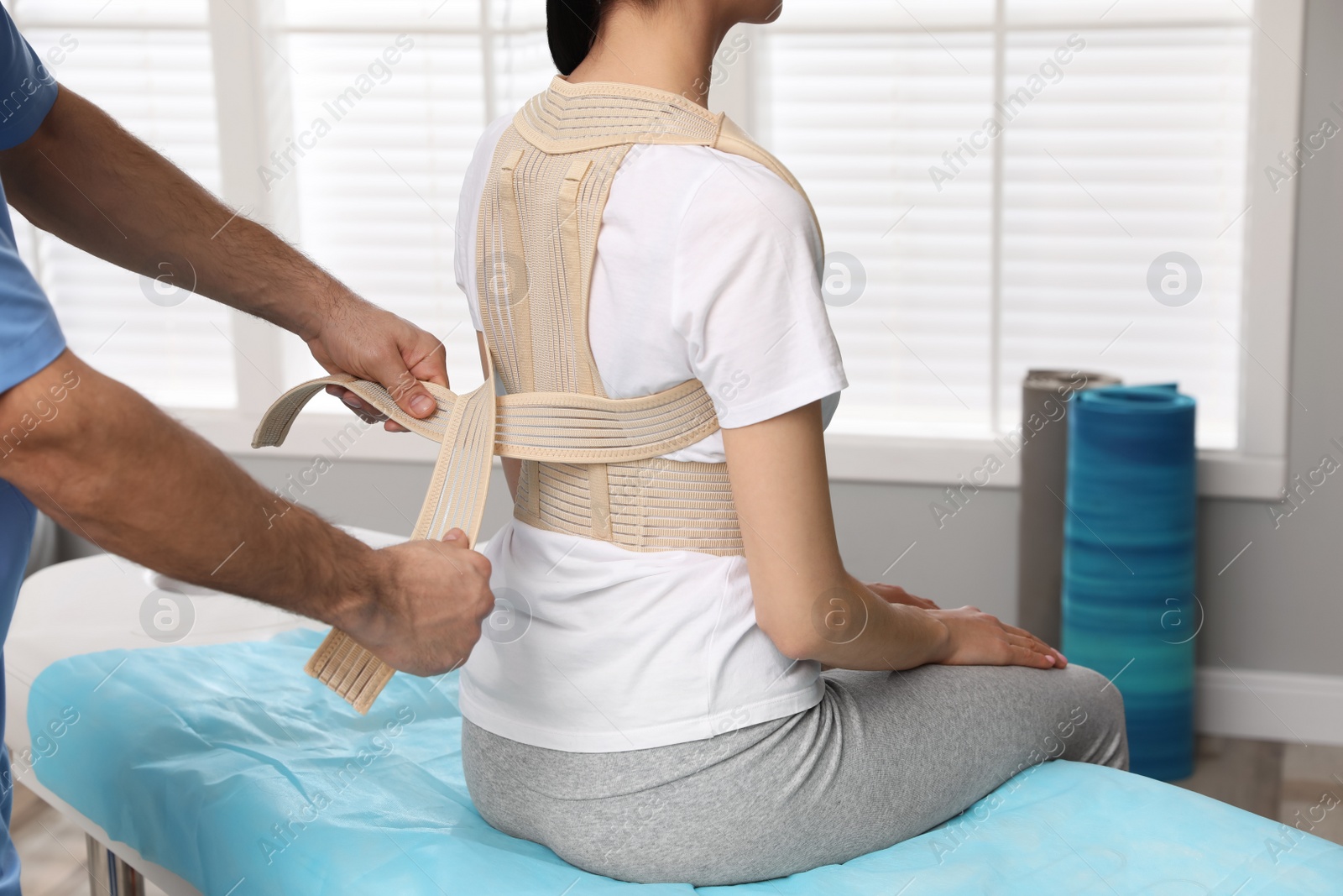 Photo of Orthopedist helping patient to put on posture corrector in clinic, closeup. Scoliosis treatment