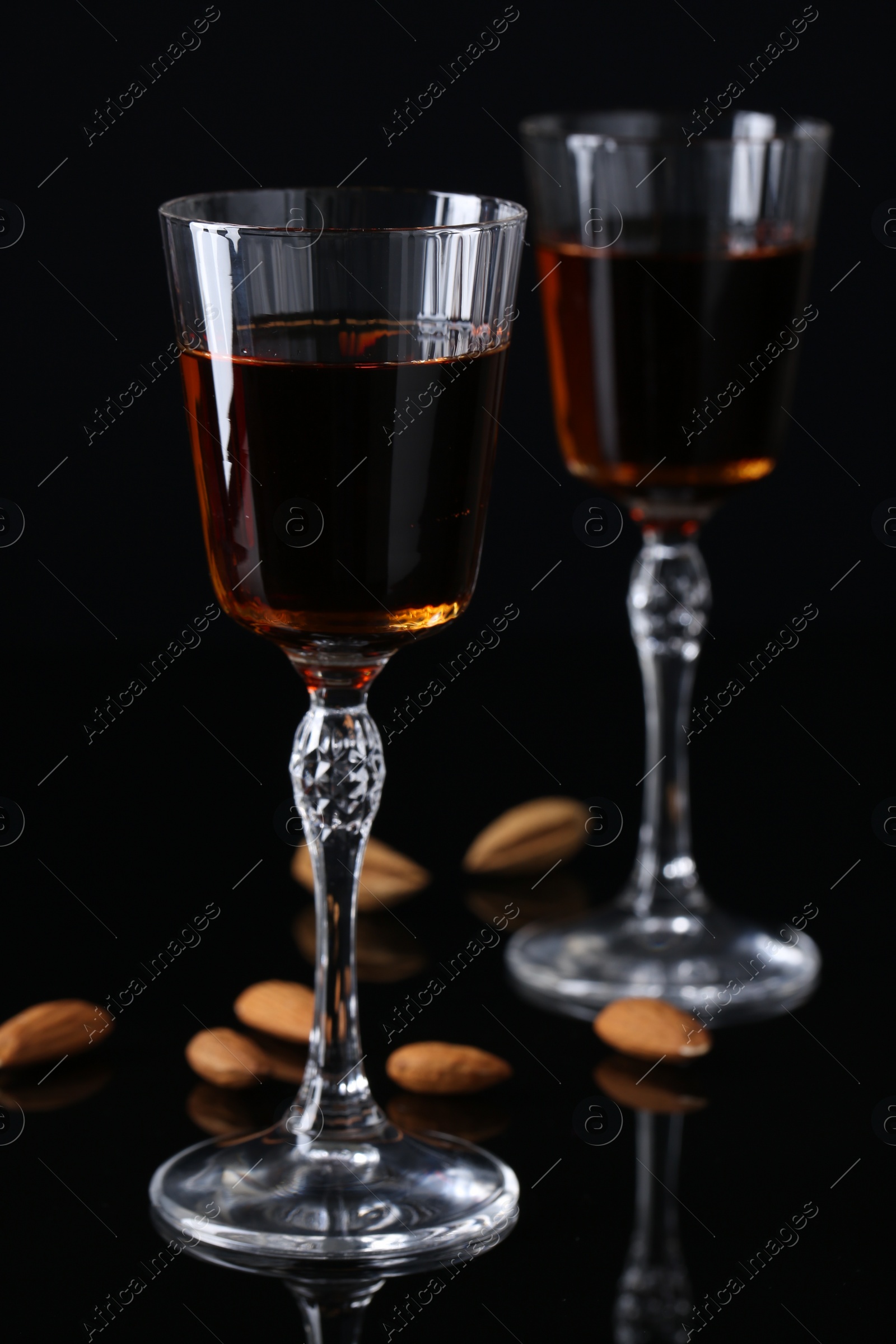 Photo of Liqueur glasses with tasty amaretto and almonds on black table, closeup