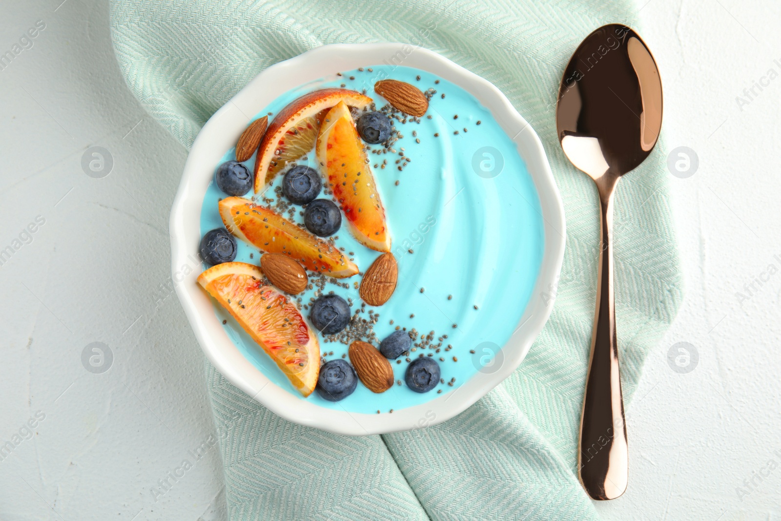 Photo of Bowl of spirulina smoothie, spoon and napkin on light table, top view
