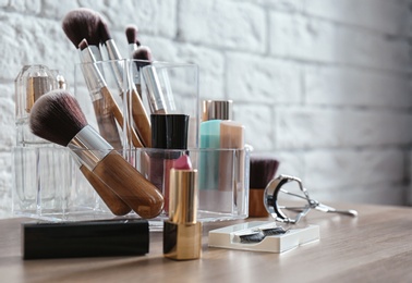 Photo of Organizer with cosmetic products for makeup on table near brick wall