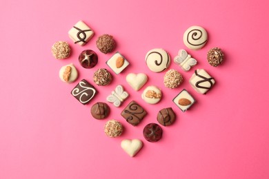 Heart made with delicious chocolate candies on pink background, top view