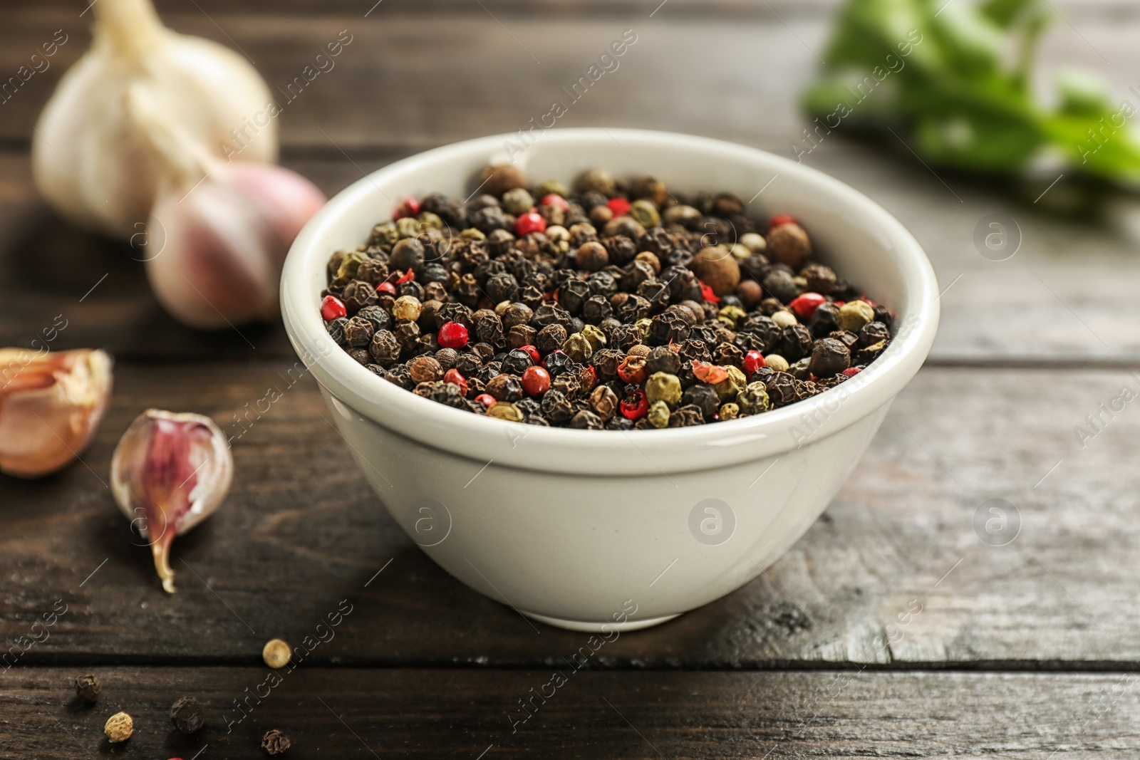 Photo of Bowl with mix of peppercorns and garlic on wooden table