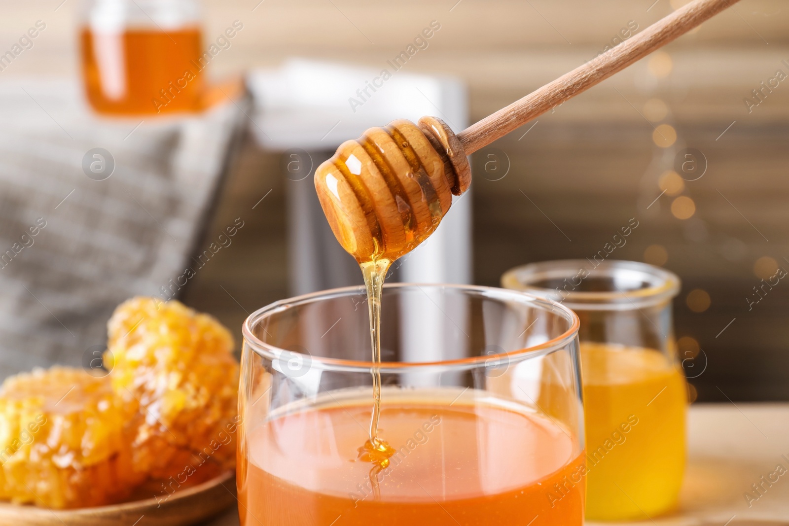 Photo of Dripping tasty honey from dipper into glass on table, closeup