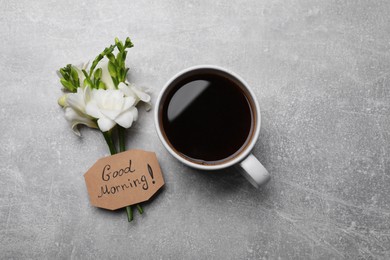 Aromatic coffee, flowers and Good Morning! message on light grey table, flat lay