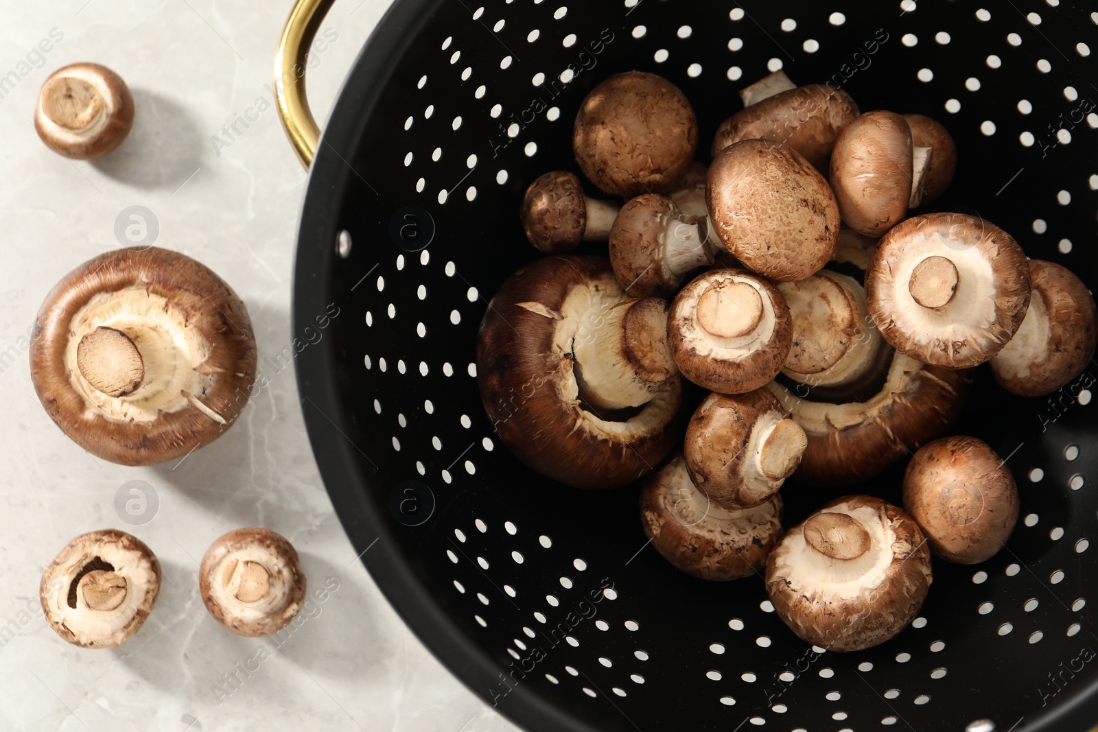 Photo of Raw mushrooms in black colander on marble table, flat lay