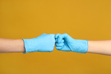 Doctors in medical gloves making fist bump on yellow background, closeup