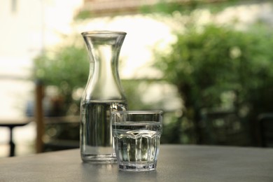 Photo of Jug and glass of fresh water on grey table outdoors
