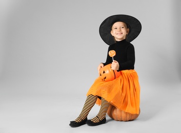 Cute little girl with pumpkin candy bucket and lollipop wearing Halloween costume on grey background. Space for text