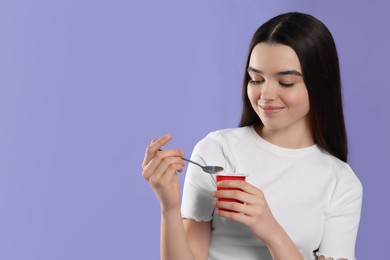 Photo of Smiling teenage girl with delicious yogurt and spoon on violet background. Space for text